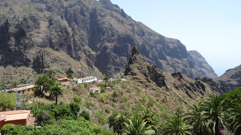 Vue panoramique des montagnes avec des formations rocheuses et des plantations de palmiers en bas.